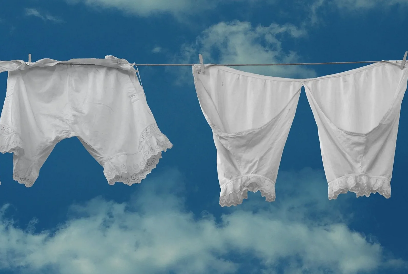 White vintage clothing drying on a clothesline with a blue sky background.